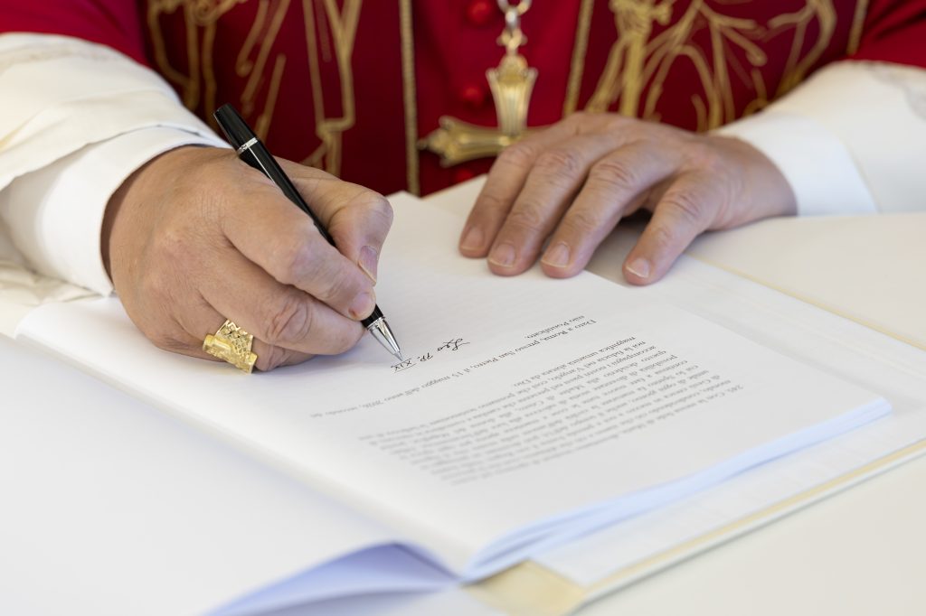Pope Leo XIV's hands holding pen signing Magnifica Humanitas encyclical letter