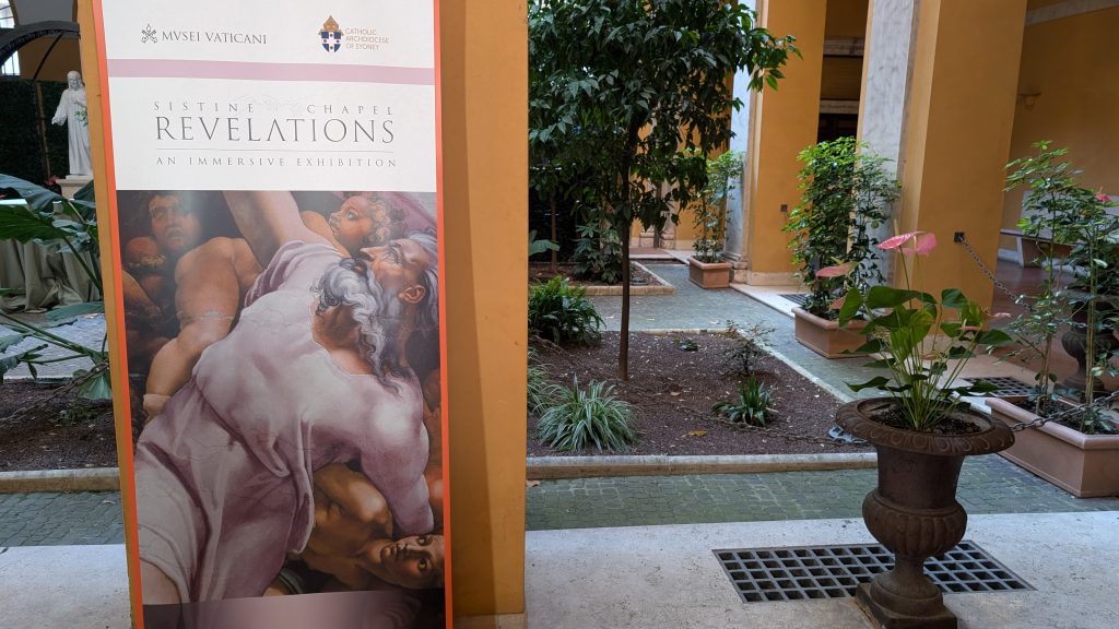 Banner at the entrance of the conference in Rome showing an image of an artwork from the Sistine Chapel and highlighting partnership between Musei Vaticani and Catholic Archdiocese of Sydney titled: REVELATIONS